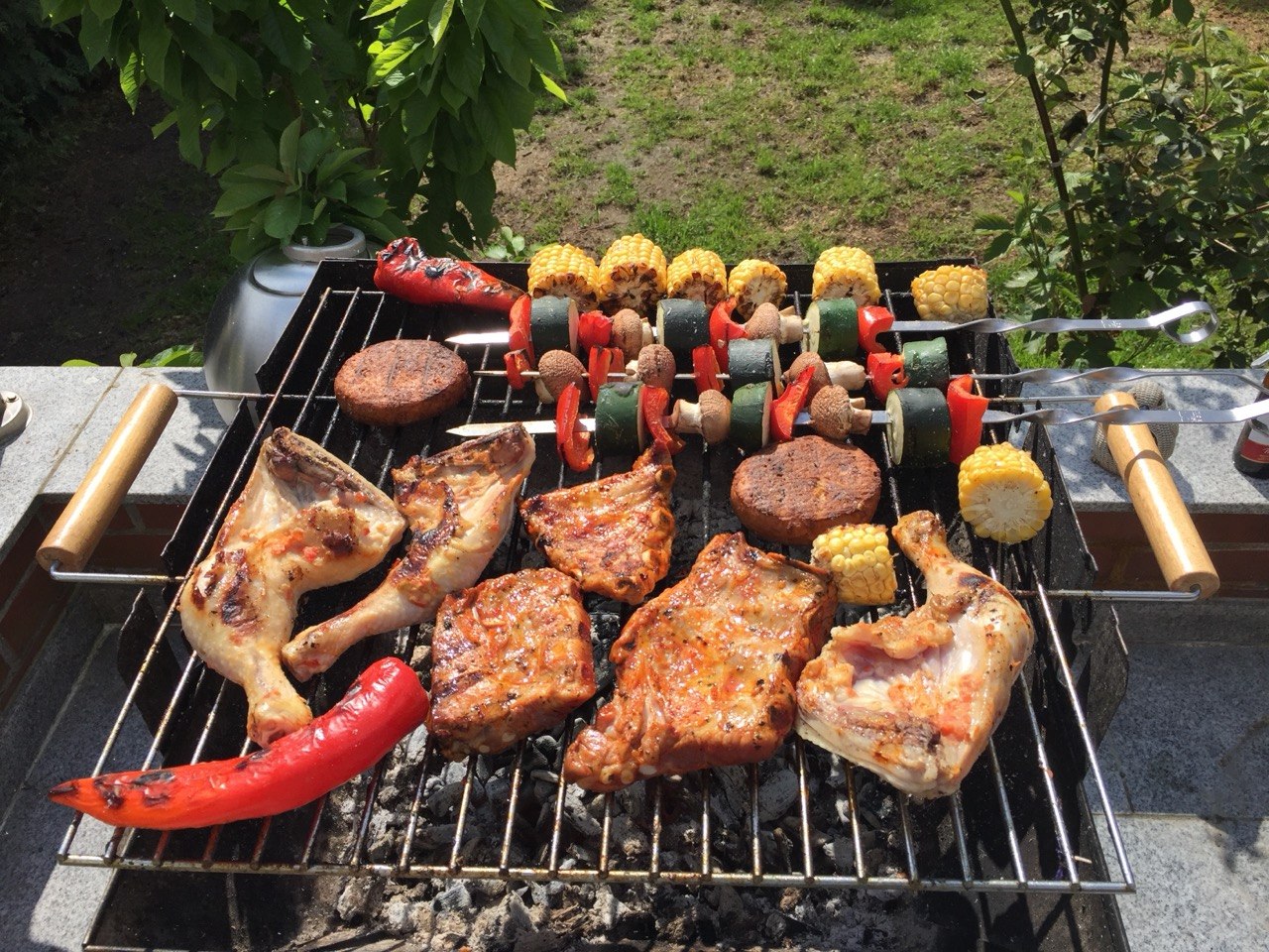 Grill mit Hähnchenschenkeln, Gemüsespießen, Mais und Burgerpattys – selbst gegrillt im Garten
