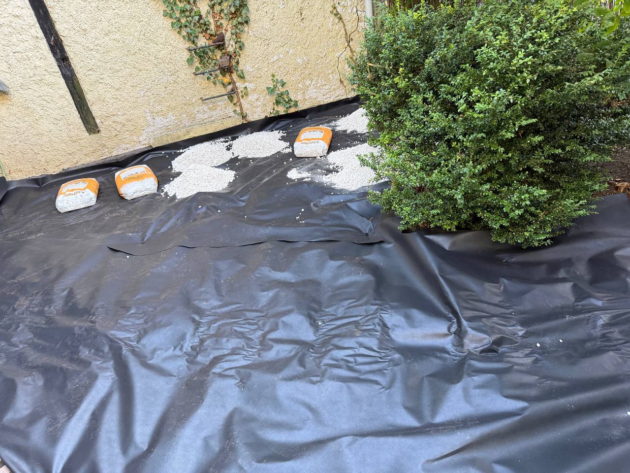 Schwarzes Unkrautvlies auf dem Gartenbeet, Säcke mit weißem Kies bereitgestellt