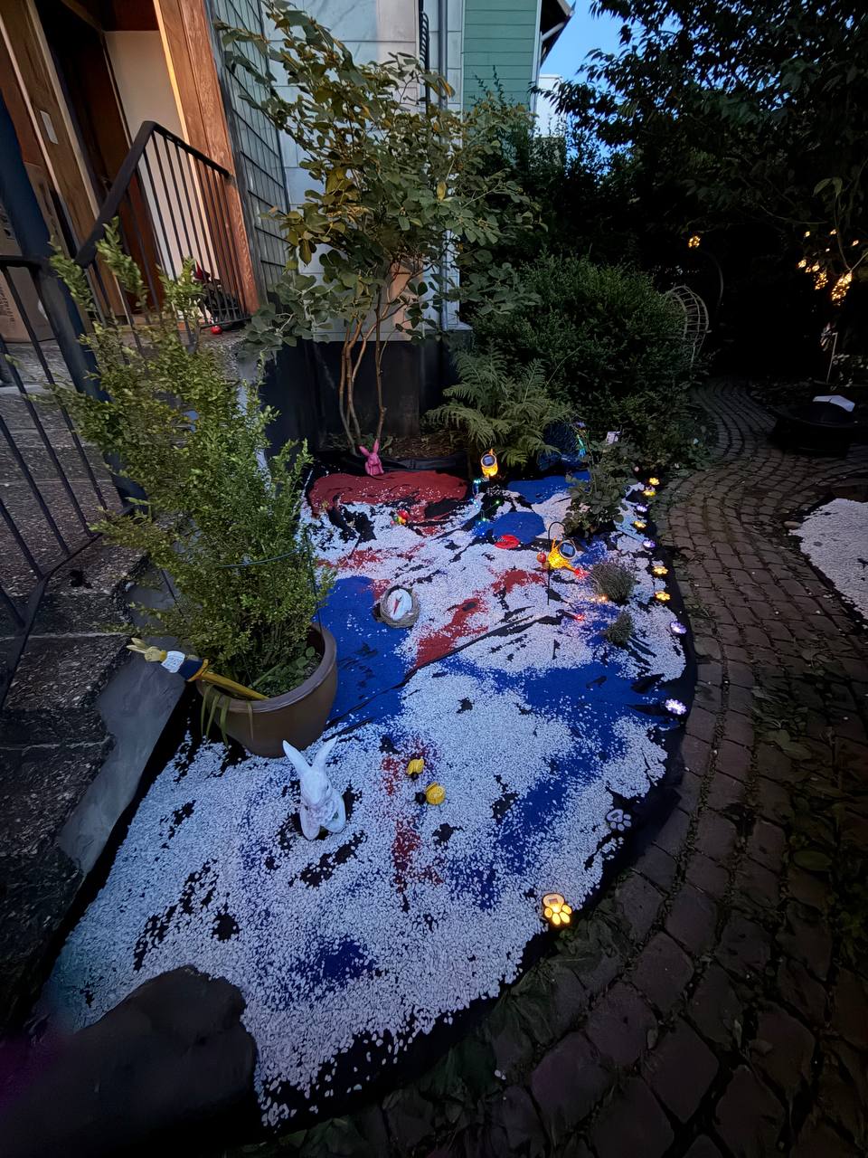 Fertig angelegtes Gartenbeet mit weißem Kies, buntem Aquariumkies und Gartenbeleuchtung am Abend