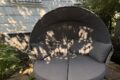 Runde Gartenliege Invicta Interiors Seattle mit Baldachin und grauen Polstern – fertig aufgebaut im kleinen Garten