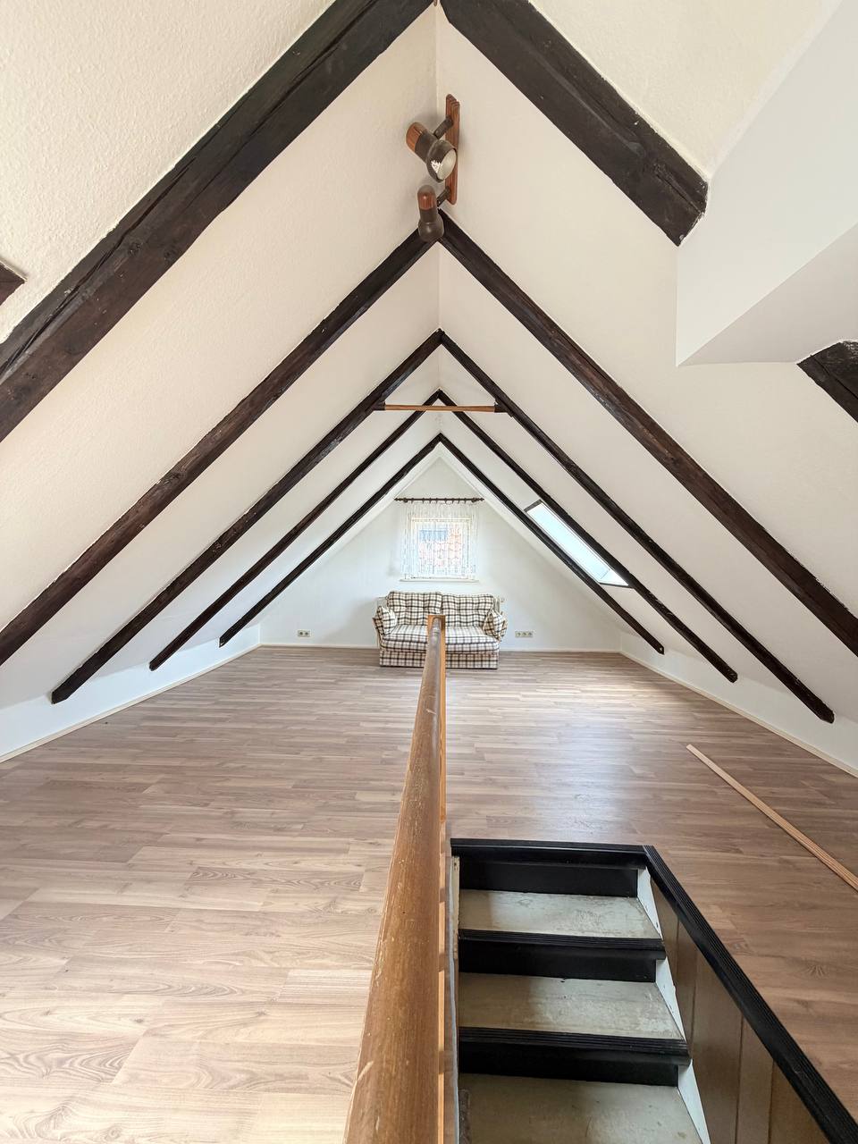 Dachbodenausbau in Eigenregie – Blick von der Treppe auf die fertige Mansarde mit Holzbalken und Laminat